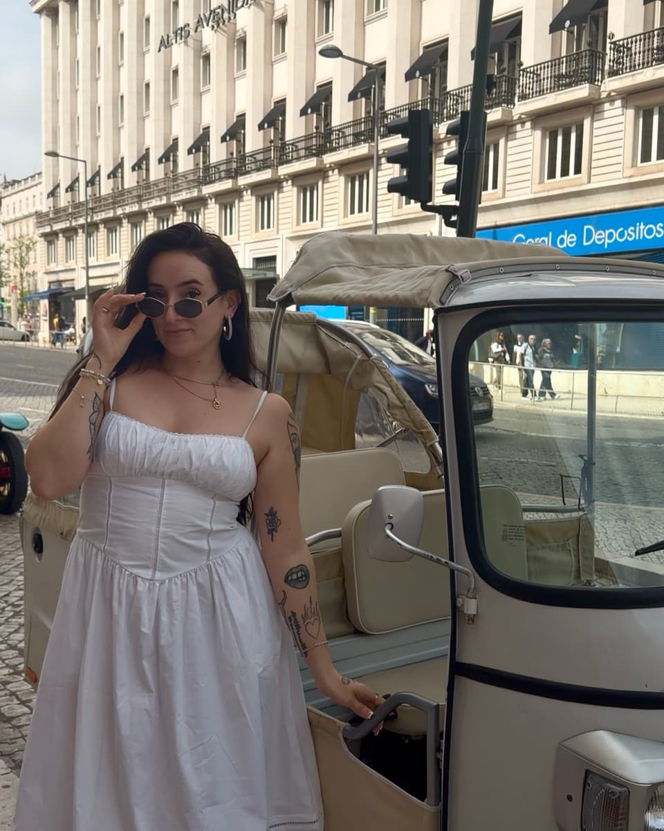 Miranda in a white dress beside a tuk tuk on a street in Lisbon