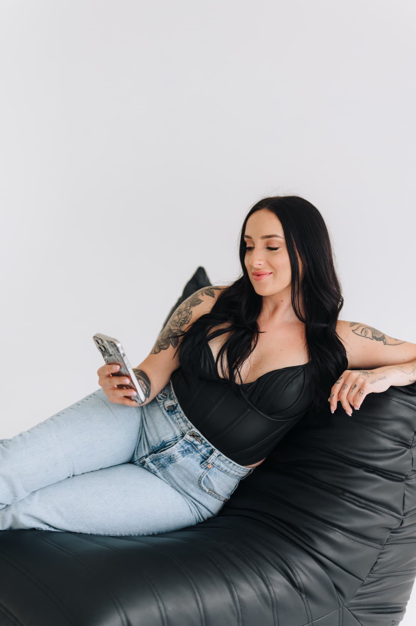 Miranda Bloch sitting on a black leather lounge chair holding her phone during a studio content shoot