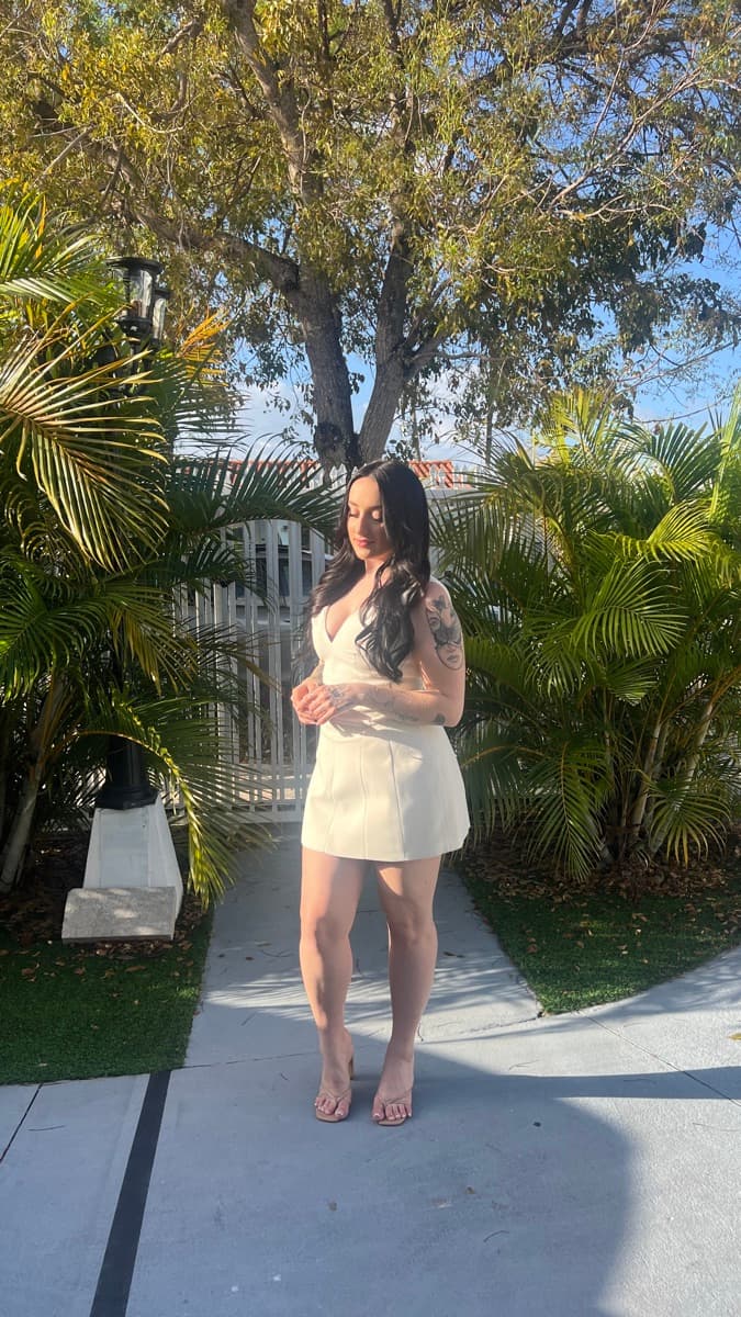 Miranda in a white outfit standing between palm trees