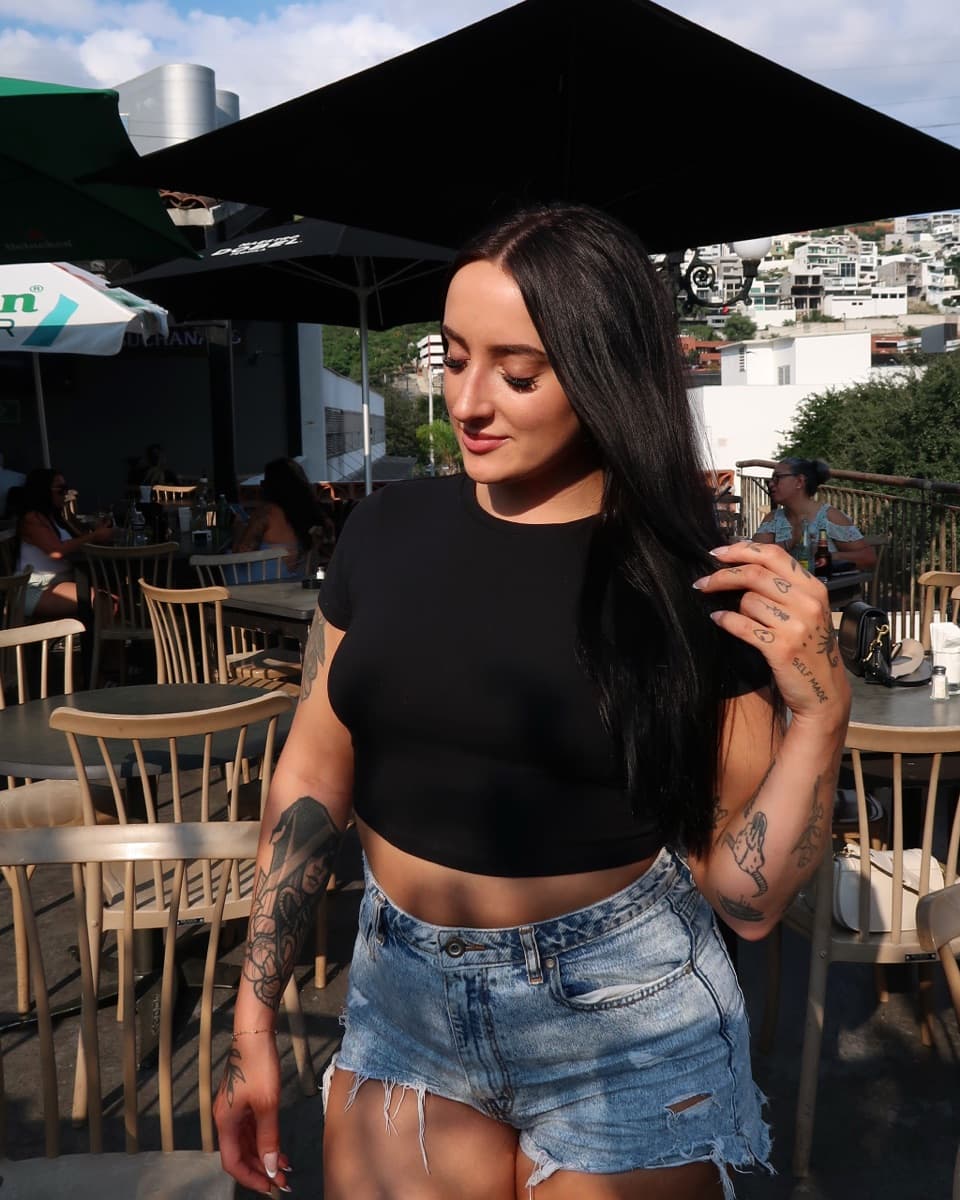 Miranda on a hillside terrace in a black crop top and denim shorts