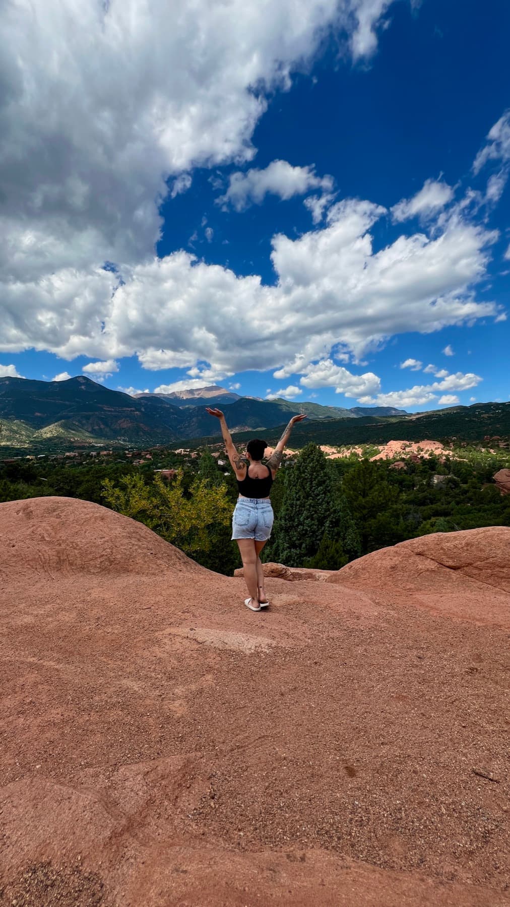 Miranda standing on red rock with her arms raised toward a mountain range under an open sky